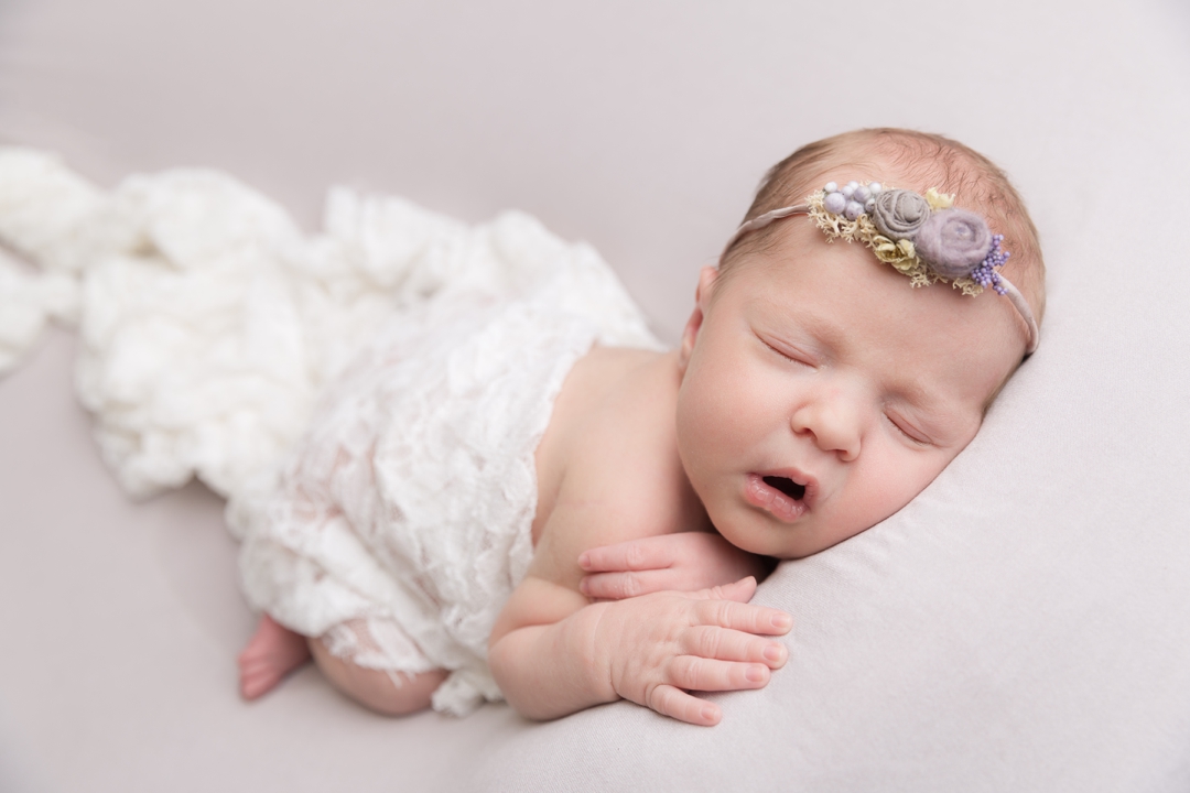 Studio newborn photography by hayley morris photography in Worcestershire baby with a headband on and wrap posed on a posing backdrop